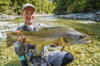 Devin Olsen holds a large brown trout while kneeling in a river.