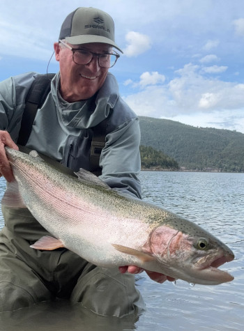 Brian O'Keefe stands in a river holding a large steelhead.